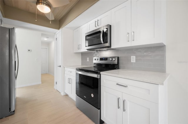 kitchen with stainless steel appliances, white cabinets, backsplash, baseboards, and a ceiling fan