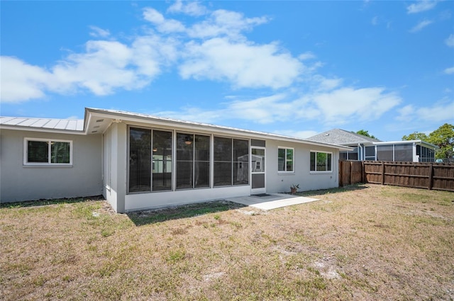 rear view of house with a standing seam roof, a sunroom, stucco siding, a yard, and a fenced backyard