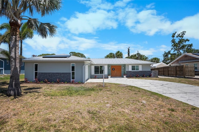 ranch-style home featuring roof mounted solar panels, concrete driveway, stucco siding, fence, and a front lawn
