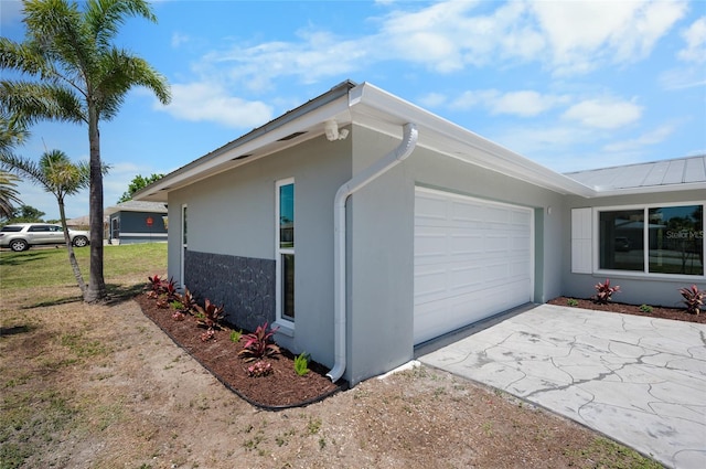 view of property exterior with stucco siding, metal roof, driveway, stone siding, and an attached garage