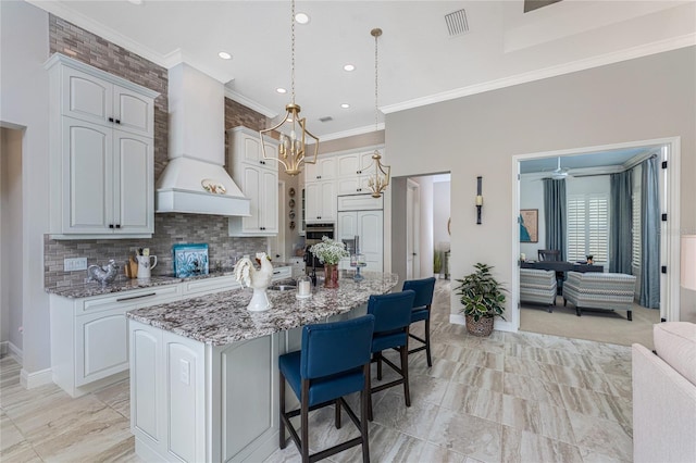 kitchen with ornamental molding, custom range hood, light stone counters, a kitchen bar, and decorative backsplash