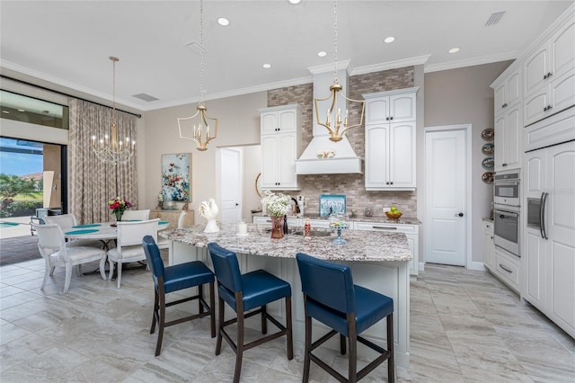 kitchen featuring a chandelier, tasteful backsplash, crown molding, an island with sink, and a breakfast bar