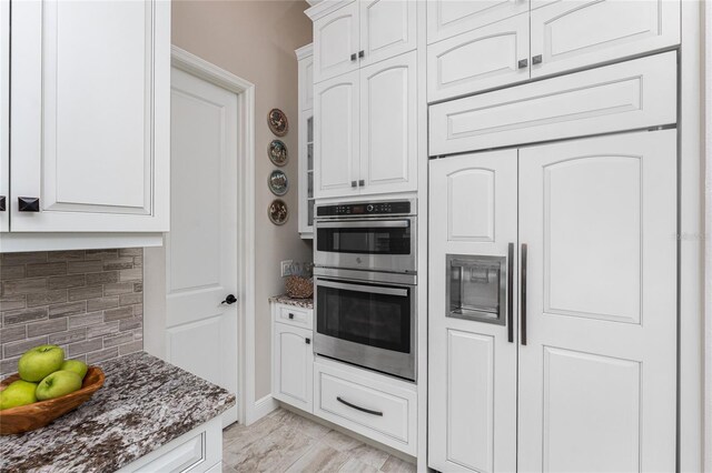 kitchen with stainless steel double oven, dark stone counters, backsplash, paneled built in fridge, and white cabinets