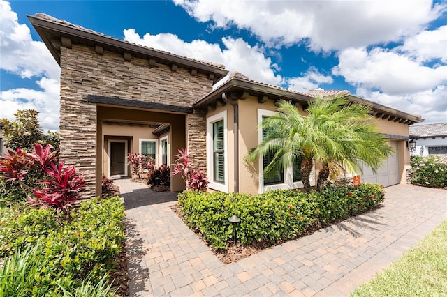 back of property with stone siding, a garage, stucco siding, and driveway