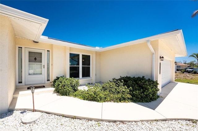 entrance to property featuring stucco siding, an attached garage, and driveway