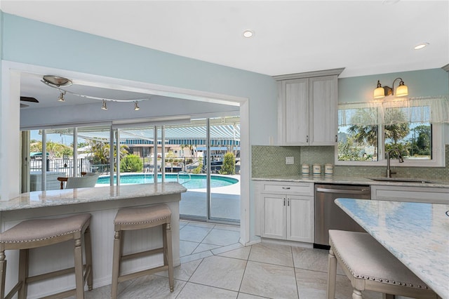 kitchen featuring stainless steel dishwasher, decorative backsplash, a kitchen bar, a sink, and a wealth of natural light