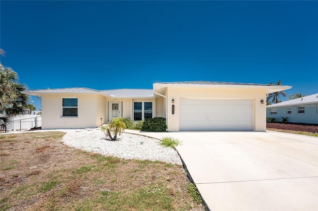 ranch-style house with stucco siding, a standing seam roof, metal roof, an attached garage, and driveway