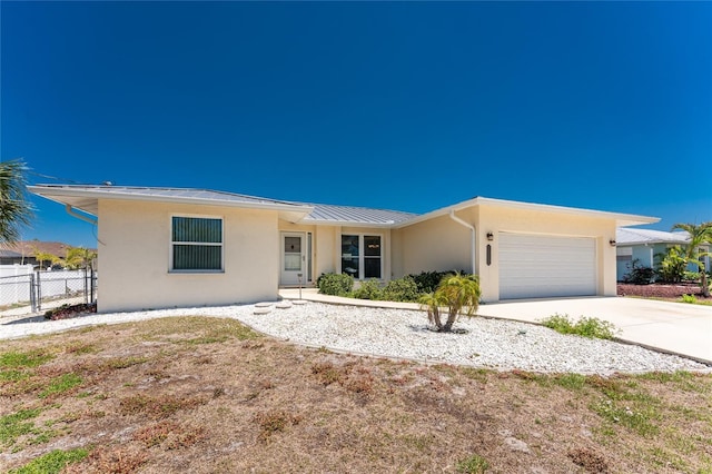single story home with fence, stucco siding, a standing seam roof, an attached garage, and driveway