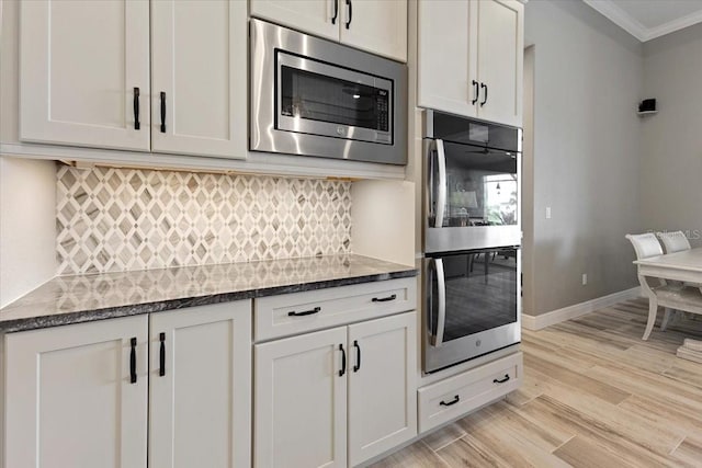 kitchen featuring crown molding, dark stone countertops, light wood-style flooring, appliances with stainless steel finishes, and backsplash