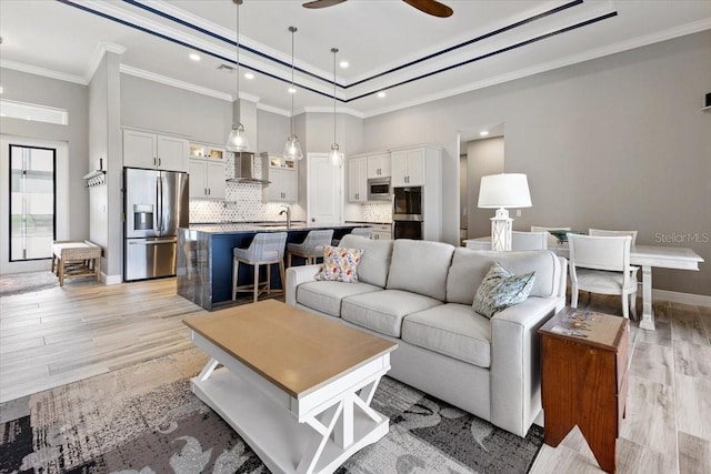 living area with a ceiling fan, crown molding, light wood-type flooring, a raised ceiling, and recessed lighting