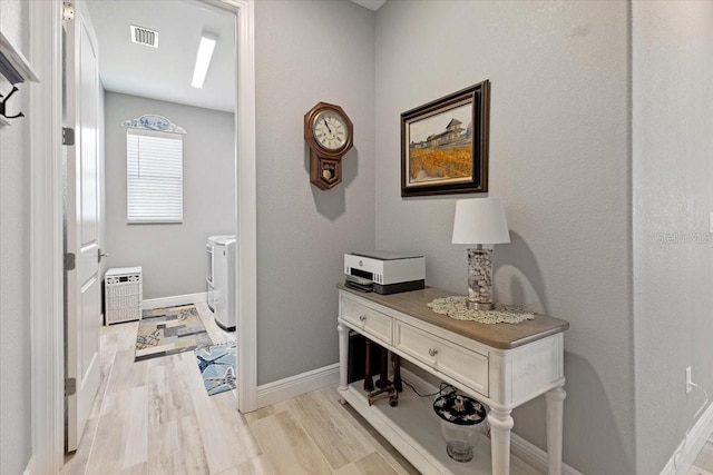 corridor featuring baseboards, visible vents, washer and clothes dryer, and light wood-type flooring