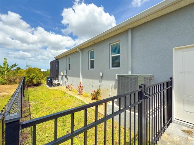 view of side of property with fence, central AC unit, stucco siding, and a yard