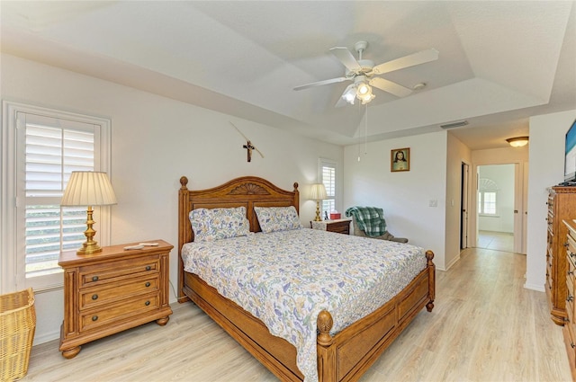 bedroom with ceiling fan, a raised ceiling, baseboards, light wood-type flooring, and visible vents