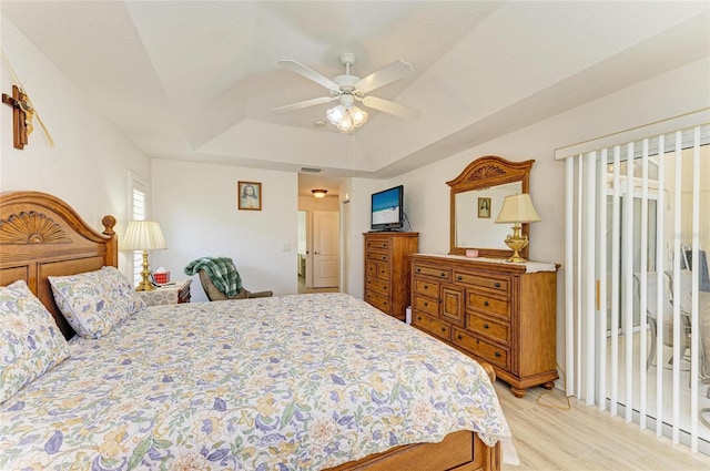 bedroom with a ceiling fan, visible vents, access to outside, a tray ceiling, and light wood-style flooring
