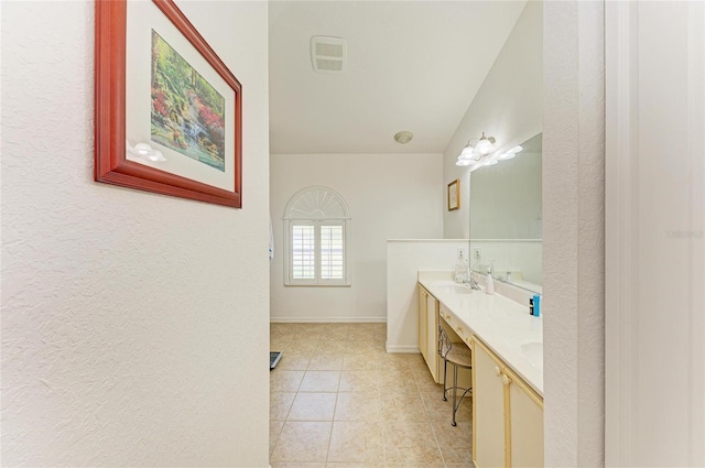 bathroom featuring a textured wall, double vanity, tile patterned floors, baseboards, and visible vents