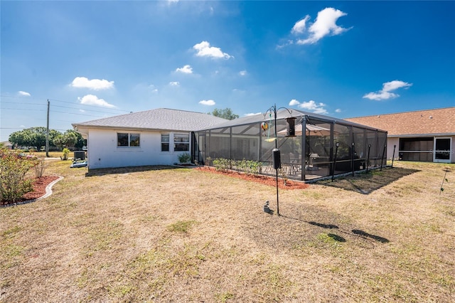 back of property featuring a lawn, stucco siding, and glass enclosure