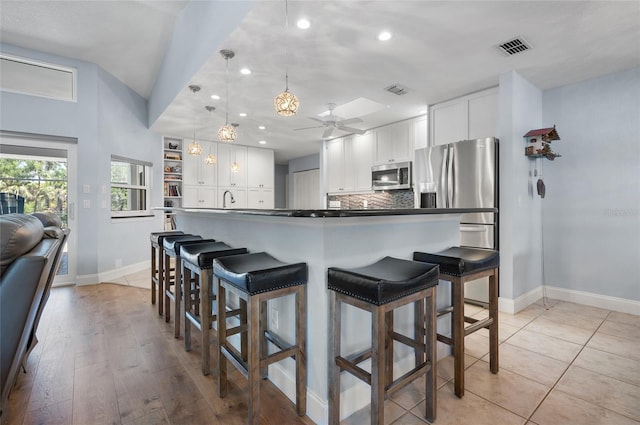 kitchen featuring a breakfast bar area, stainless steel appliances, white cabinetry, visible vents, and ceiling fan