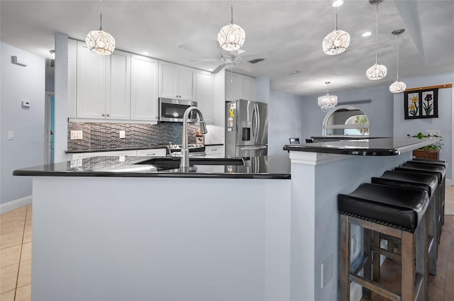kitchen with ceiling fan with notable chandelier, dark countertops, stainless steel appliances, baseboards, and backsplash