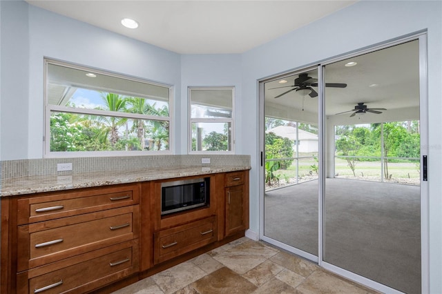 1155 Osceola Blvd, Englewood, FL 34223 - kitchen with stainless steel microwave, brown cabinets, light stone counters, stone finish floor, and recessed lighting