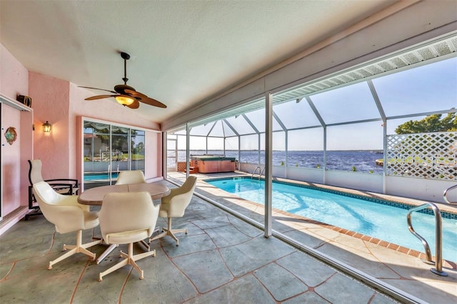 outdoor pool with ceiling fan, a patio area, a hot tub, glass enclosure, and a water view