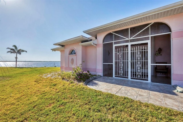 doorway to property with a lawn, a water view, and stucco siding