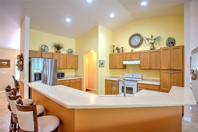 kitchen featuring a breakfast bar area, under cabinet range hood, arched walkways, baseboards, and appliances with stainless steel finishes