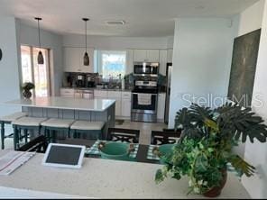 4093 Pelican Shores Cir, Englewood, FL 34223 - kitchen featuring stainless steel appliances, white cabinets, decorative light fixtures, a breakfast bar, and light countertops