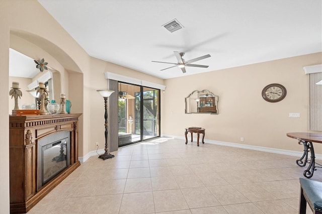 living area with ceiling fan, light tile patterned floors, a glass covered fireplace, and baseboards