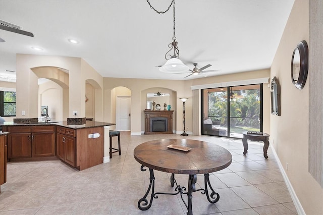 living area with ceiling fan, a fireplace, arched walkways, baseboards, and light tile patterned floors