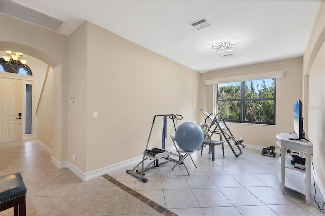 exercise area featuring arched walkways, a chandelier, baseboards, and light tile patterned floors