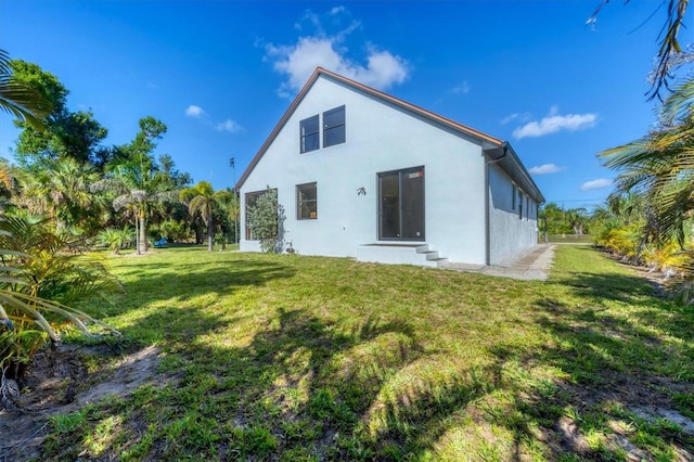 back of property featuring stucco siding, a yard, and entry steps