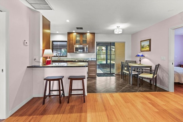 7180 Quarry St, Englewood, FL 34224 - kitchen featuring stainless steel microwave, dark countertops, glass insert cabinets, a sink, and a breakfast bar