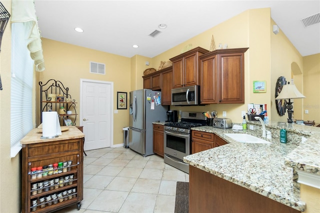 142 Savona Way N, Venice, FL 34275 - kitchen featuring stainless steel appliances, a sink, a peninsula, light stone countertops, and brown cabinets