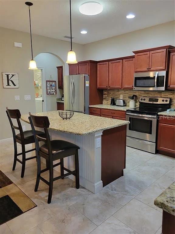 142 Yellow Pine Dr, Rotonda West, FL 33947 - kitchen featuring stainless steel appliances, tasteful backsplash, a center island, and light stone counters