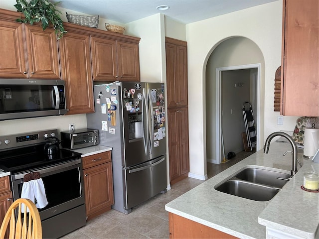 kitchen with stainless steel appliances, a sink, light tile patterned flooring, brown cabinets, and light countertops