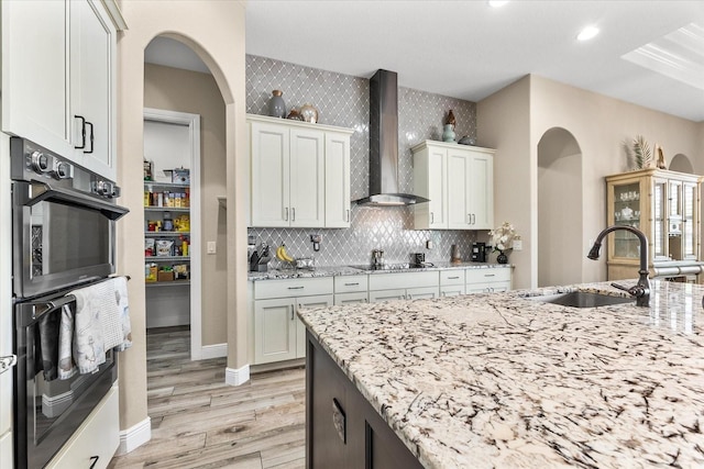 15044 San Domingo Blvd, Port Charlotte, FL 33981 - kitchen with wall chimney range hood, a sink, light wood-style floors, arched walkways, and light stone counters