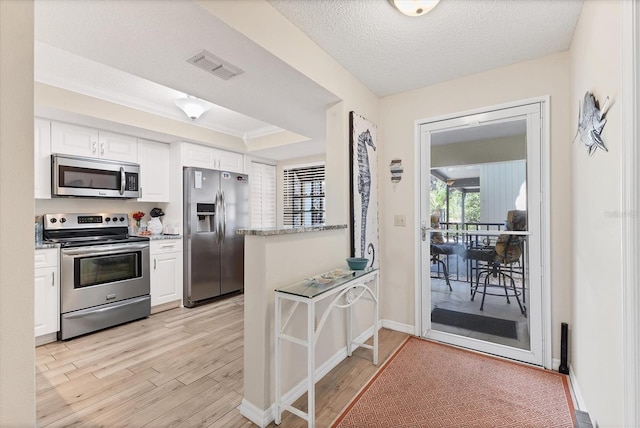 507 Pine Hollow Cir Unit 507, Englewood, FL 34223 - kitchen with appliances with stainless steel finishes, white cabinetry, light wood-style flooring, a peninsula, and a raised ceiling