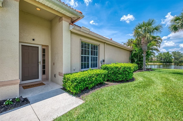 2692 Wax Myrtle Ct, Port Charlotte, FL 33953 - view of exterior entry with stucco siding, a yard, and a water view