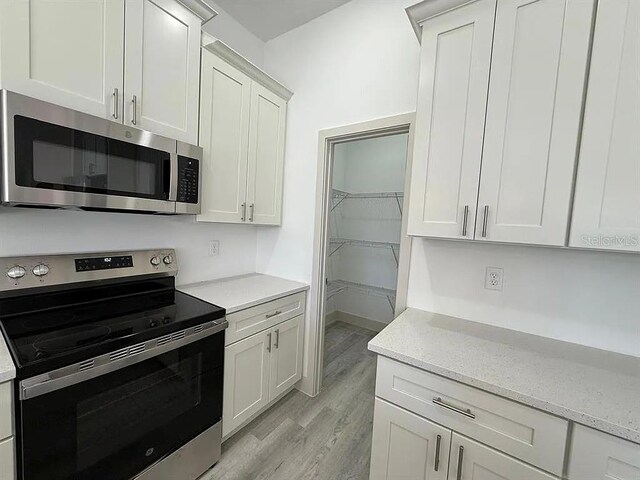 18043 Hillsborough Blvd, Port Charlotte, FL 33954 - kitchen featuring appliances with stainless steel finishes, light wood-style floors, light stone countertops, and white cabinetry