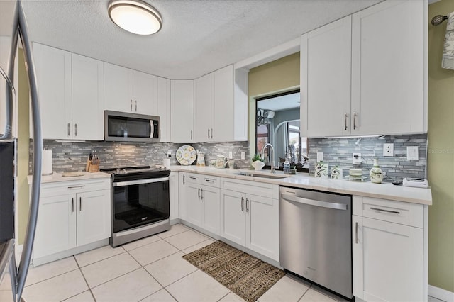 kitchen featuring appliances with stainless steel finishes, light countertops, a sink, white cabinetry, and a textured ceiling