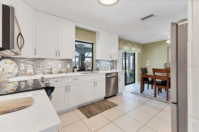 kitchen featuring stainless steel appliances, a sink, decorative backsplash, white cabinetry, and a textured ceiling