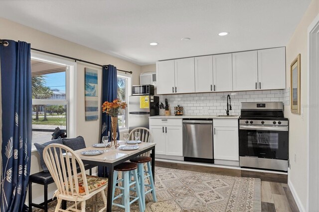 115 Friendship Ln, Englewood, FL 34223 - kitchen with stainless steel appliances, a sink, light wood-style flooring, backsplash, and white cabinetry
