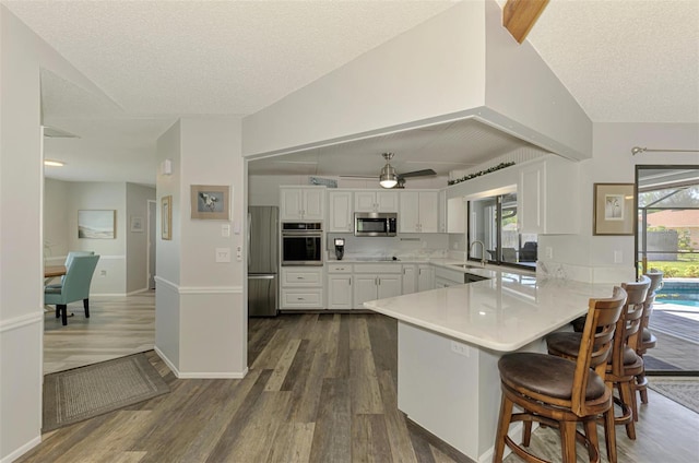 9869 Gulfstream Blvd, Englewood, FL 34224 - kitchen with appliances with stainless steel finishes, dark wood-type flooring, a peninsula, a sink, and white cabinetry