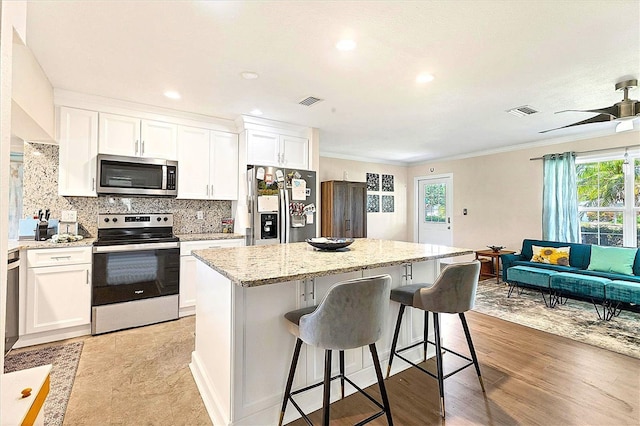 305 E Wentworth Cir, Englewood, FL 34223 - kitchen featuring appliances with stainless steel finishes, ornamental molding, a center island, backsplash, and a kitchen breakfast bar