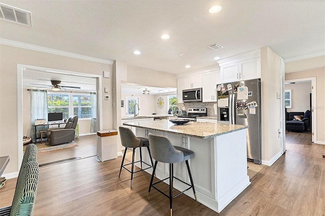 305 E Wentworth Cir, Englewood, FL 34223 - kitchen featuring stainless steel appliances, light wood-type flooring, white cabinetry, ornamental molding, and a center island