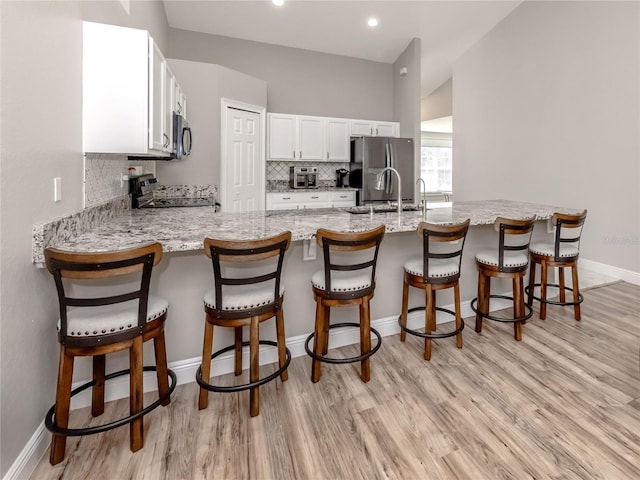 3695 Waffle Ter, North Port, FL 34286 - kitchen with stainless steel appliances, tasteful backsplash, light wood-style flooring, white cabinetry, and a peninsula