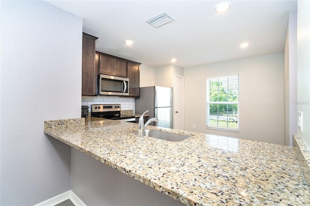 2408 Bonanza Ln, North Port, FL 34286 - kitchen with appliances with stainless steel finishes, a sink, dark brown cabinetry, a peninsula, and light stone counters