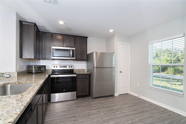 2408 Bonanza Ln, North Port, FL 34286 - kitchen featuring appliances with stainless steel finishes, a sink, dark brown cabinets, light wood-style flooring, and light stone counters