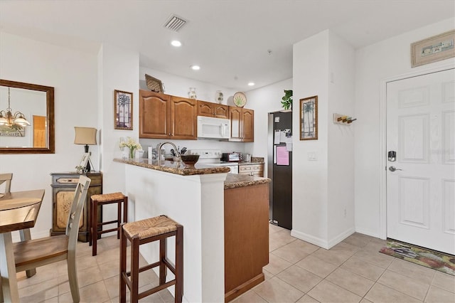 8411 Placida Rd Unit 404, Placida, FL 33946 - kitchen with white appliances, brown cabinets, a kitchen breakfast bar, light tile patterned floors, and a peninsula