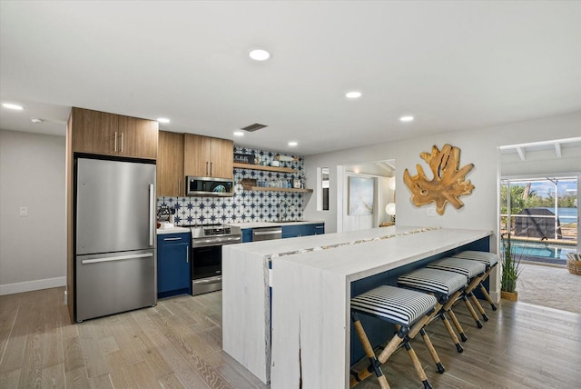 7530 Whitcomb St, Englewood, FL 34223 - kitchen with appliances with stainless steel finishes, open shelves, light wood finished floors, decorative backsplash, and a kitchen bar